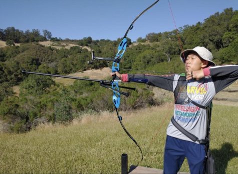 Sean Yu at practice posing with his bow and arrow ready to hit the target
